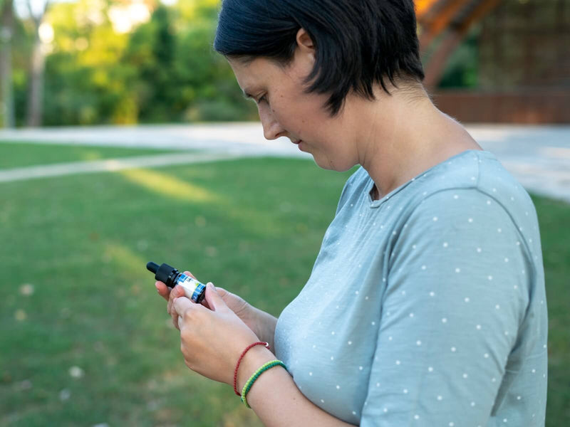 Sieviete ārā skatās uz Formula Swiss CBD eļļas pudelīti savā rokā